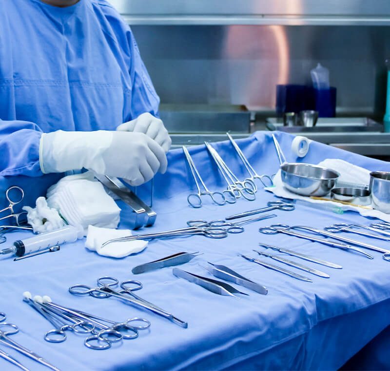 A surgical sterile processing technician wearing gloves and scrubs organizes and inspects surgical instruments laid out on a sterile drape in a hospital central-sterile department.