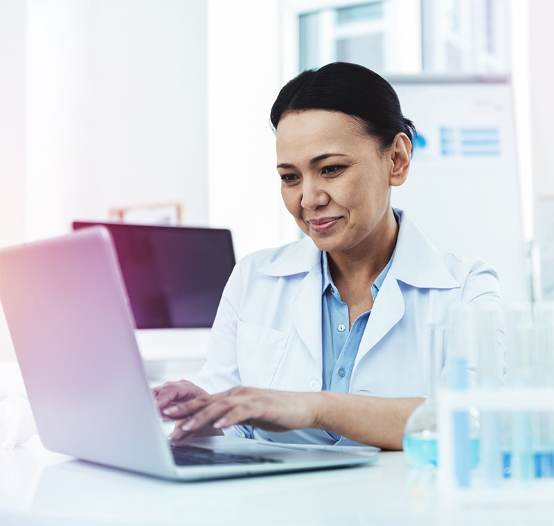 A clinical medical assistant and scribe works alongside a doctor in a bright exam room, recording patient information on a tablet while assisting with clinical tasks.